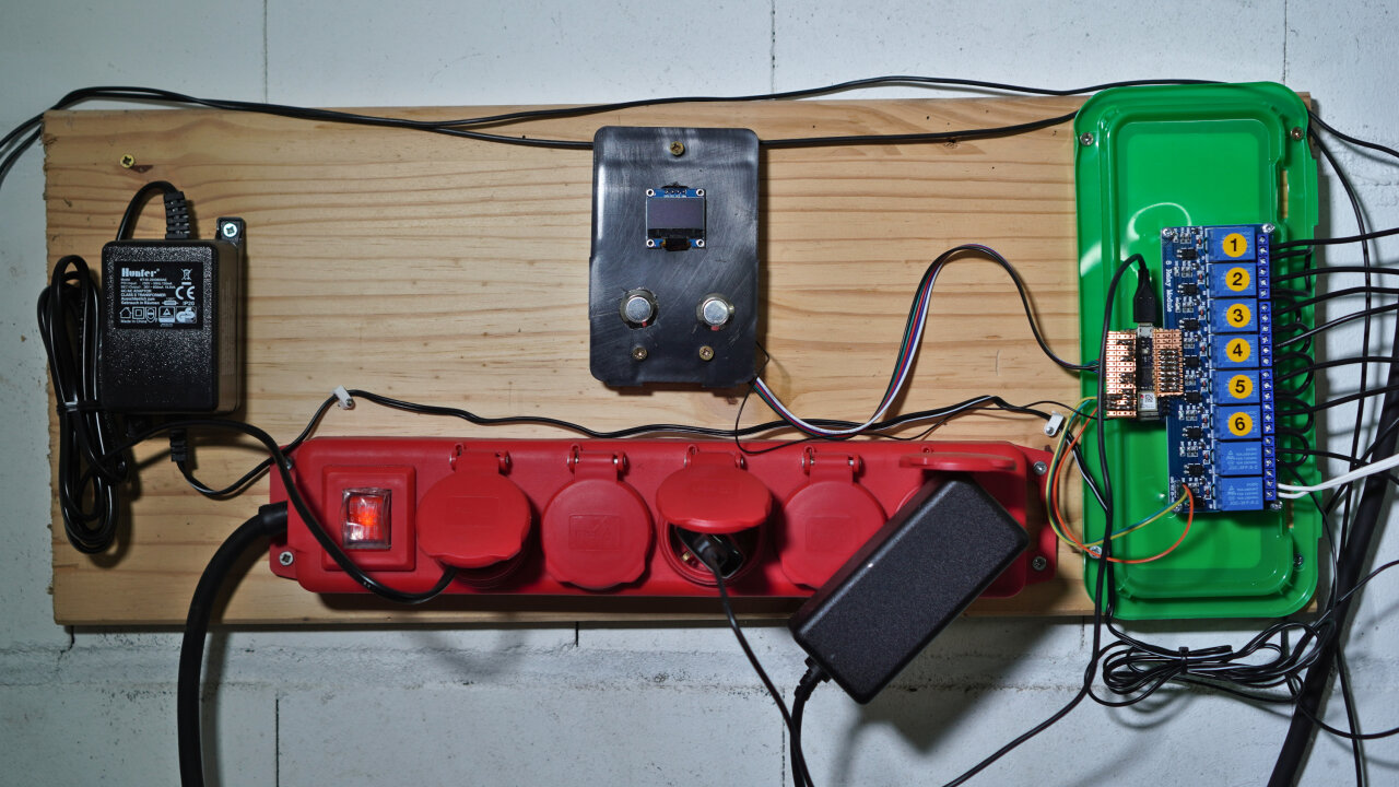 Overview of power-outlets, a power supply, a small screen with two buttons and an Arduino with a board with eight relays. All mounted on a board.