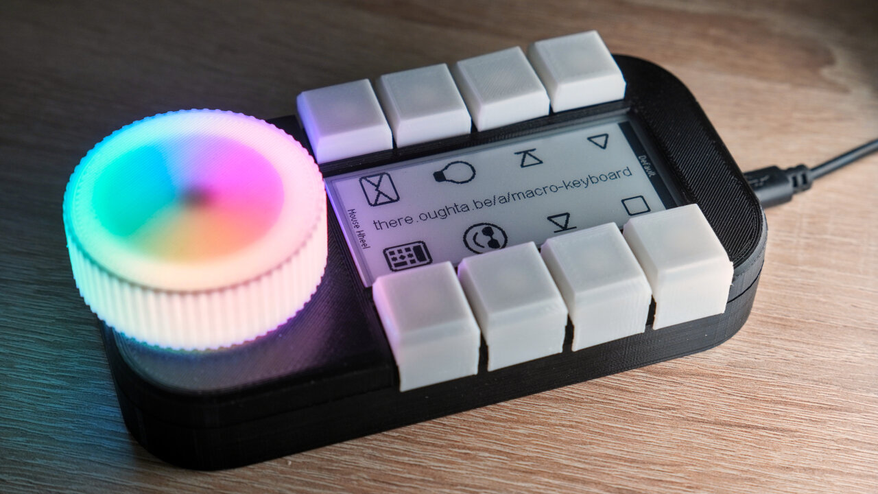 Photo of the device. On the front left there is a big knob illuminated from the back in rainbow colors. The main part of the device is dominated by a long e-ink display with four buttons on each side.