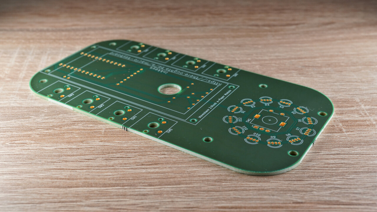 Photo of the PCB. Is rectangular with rounded corners and a hole in its center.