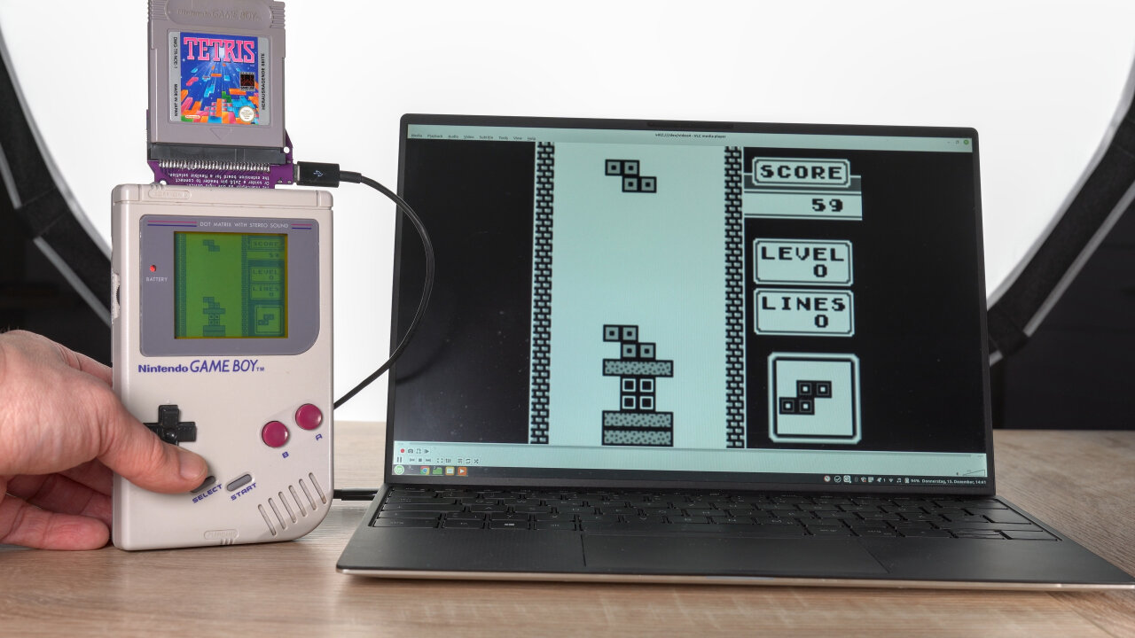 Photo of a classical Game Boy with the GB Interceptor sticking out from the top and a Tetris cartridge inserted. The Interceptor is connected to a laptop, showing the same scene of Tetris as the Game Boy's screen.