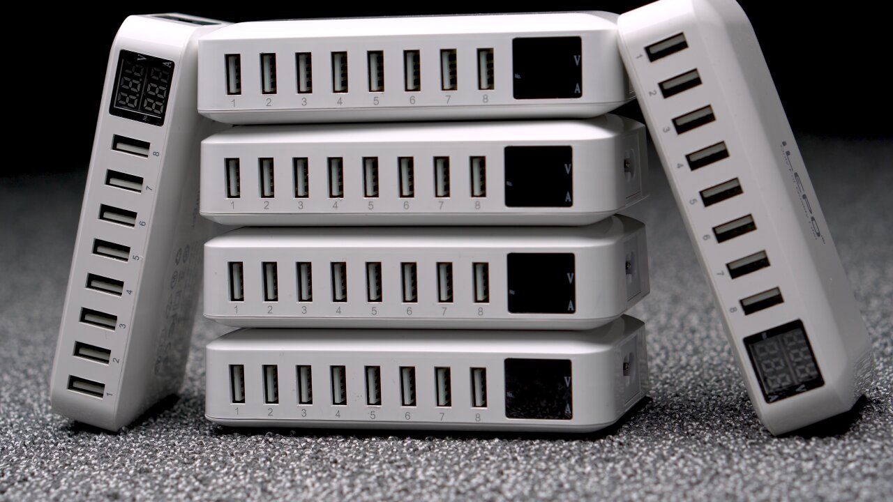 Photo of a stack of six white mutli-chargers. Each has six USB ports and a little display indicating voltage and current.