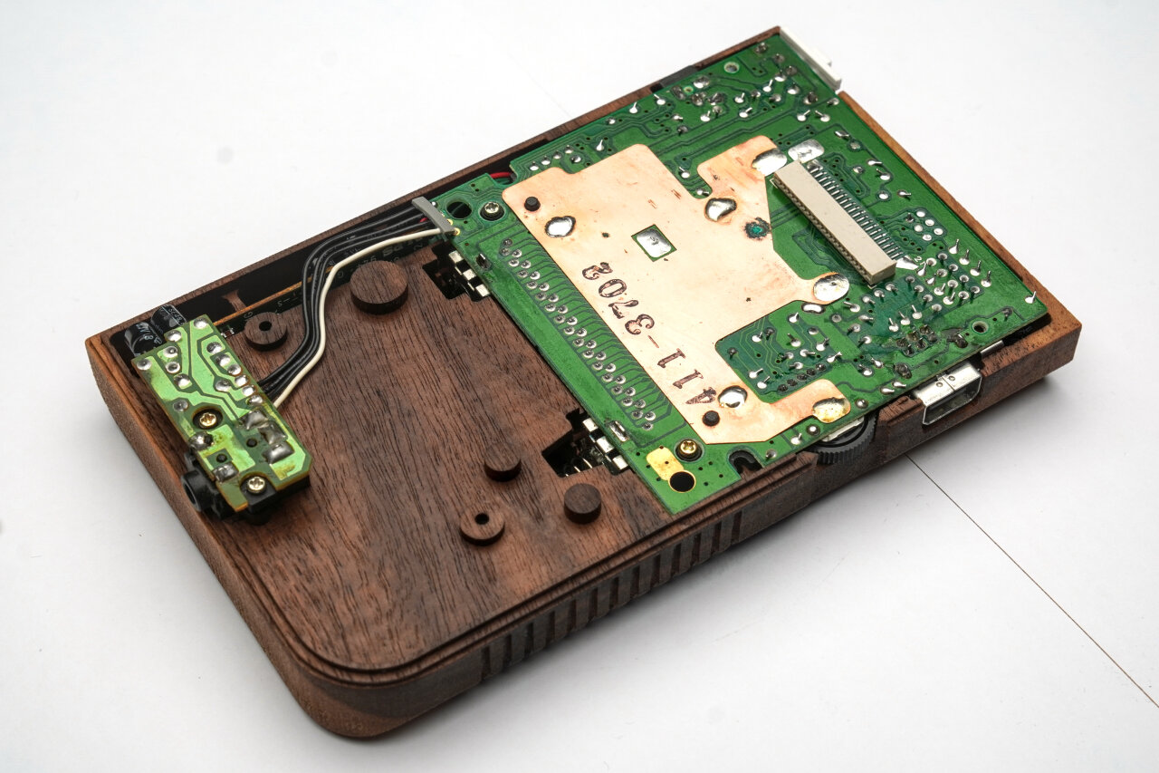 Photo of the bottom half of the wooden Game Boy shell. Large parts are covered by a green PCB, which is the main board from an original Game Boy.