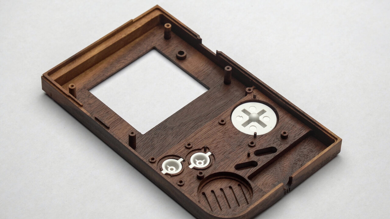 Photo of the top half of the wooden Game Boy shell. Only a white D-pad and A and B buttons have been placed in there.